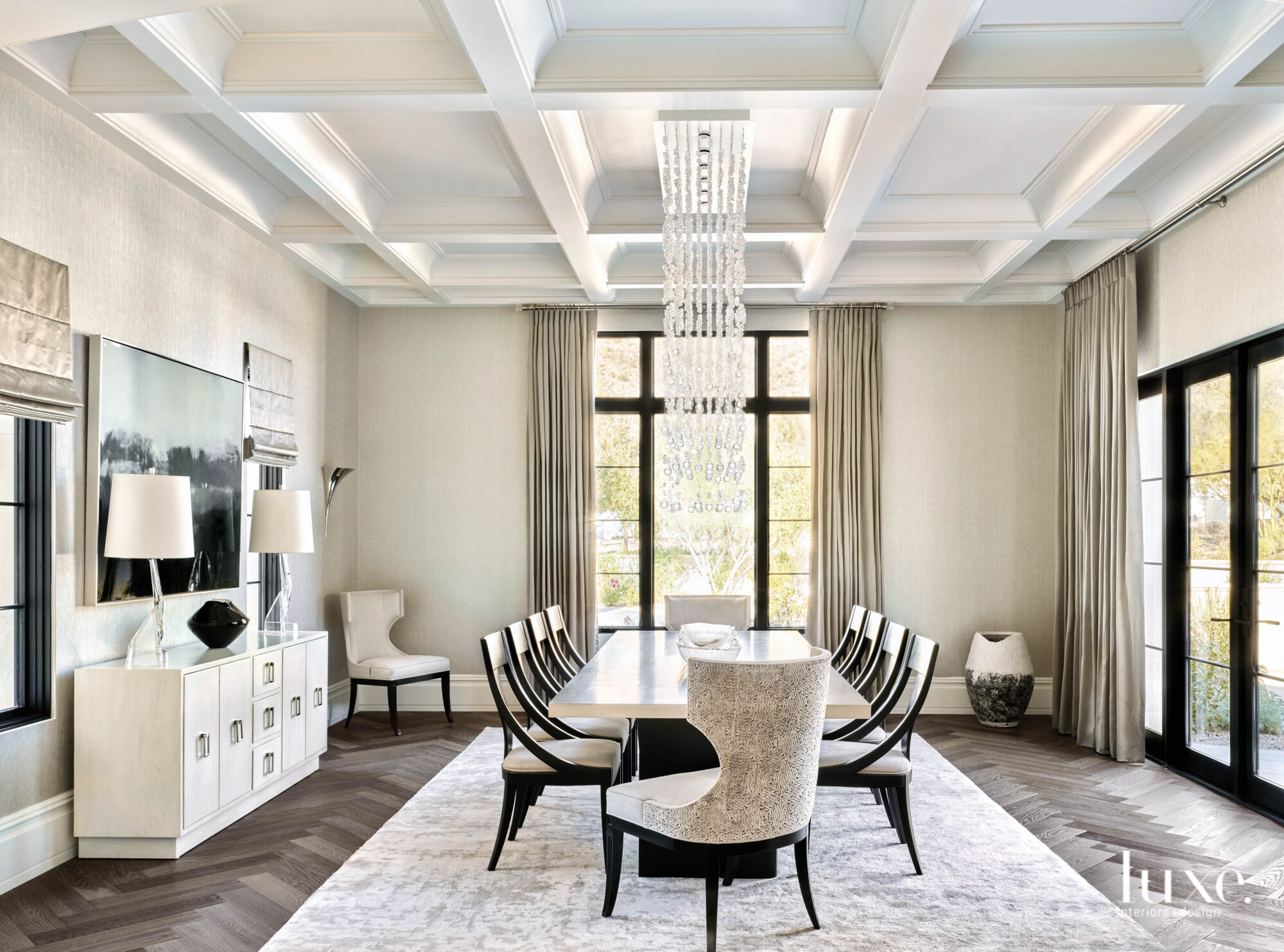 A dramatic chandelier hangs above the 10-person dining table in the dining room, which has coffered ceilings and is decorated in neutral creams and whites.