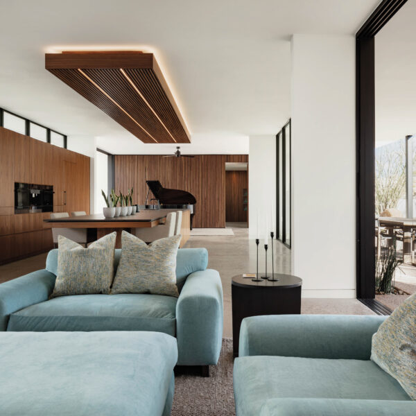 Landscape Takes The Lead In This Arizona Desert Hideaway The great room features a simple pale blue seating arrangement. The kitchen has wood cabinetry that blends with the wall.