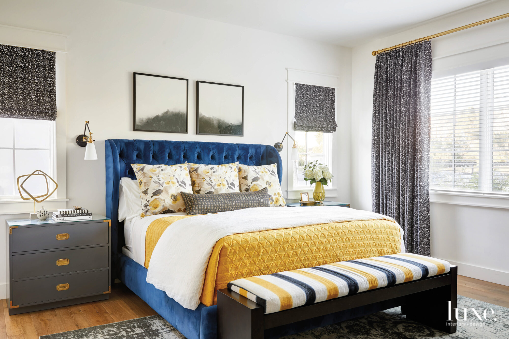 The bedroom has a blue velvet upholstered bed with yellow, blue and white linens.