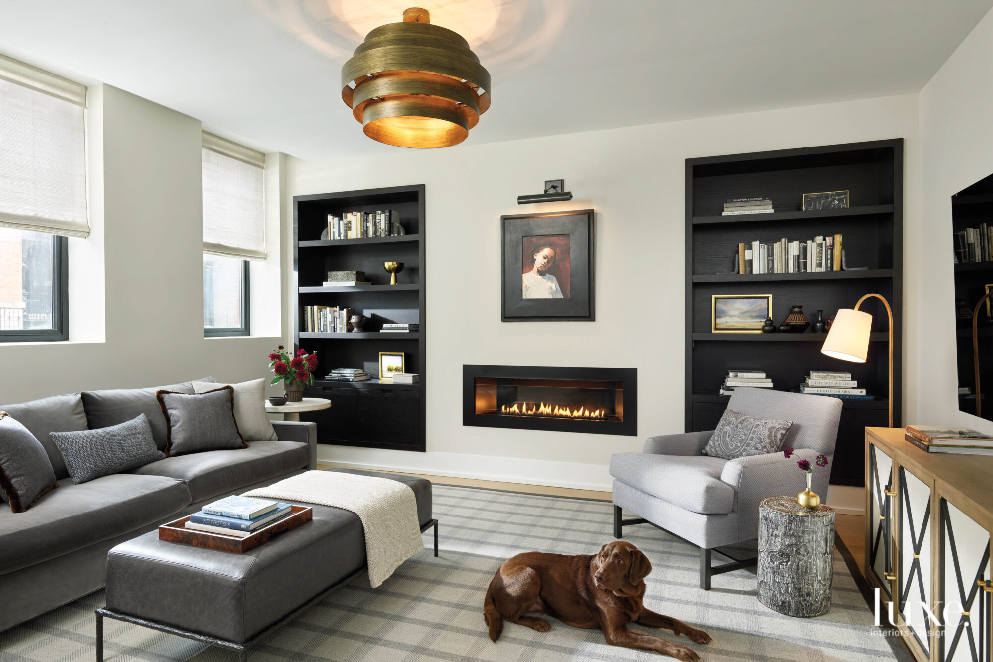 The den is decorated in shades of gray and cream with a watercolor portrait hanging above a modern inset fireplace.