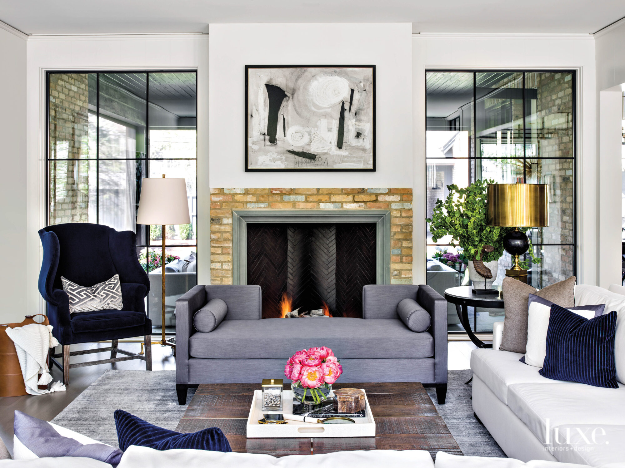 A gray chaise sits in front of a fireplace in the living room. Above it hangs an abstract painting by Graham Harmon.