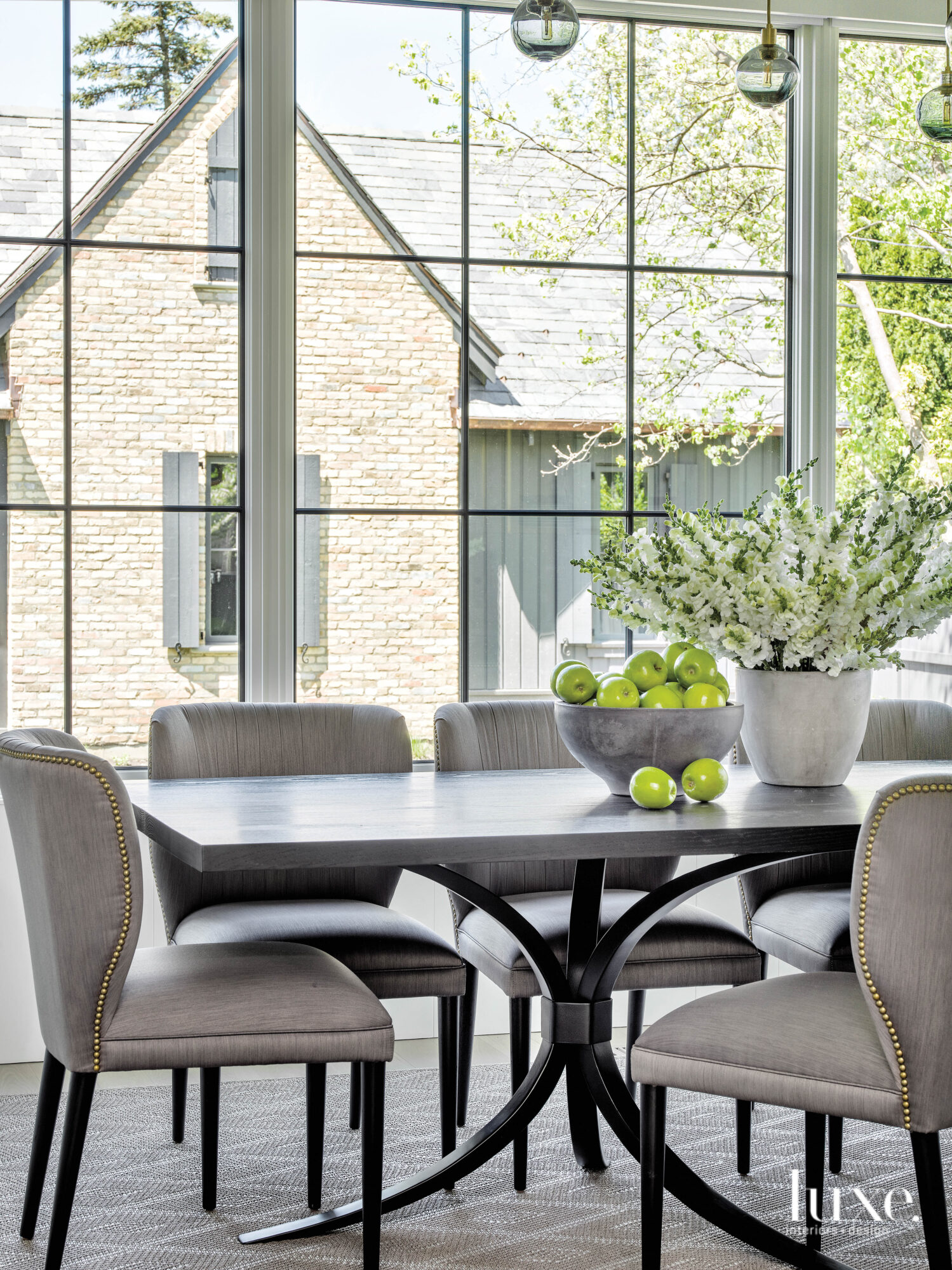 The breakfast room which looks out through floor-to-ceiling windows, is furnished with a gray dining table and gray upholstered chairs.