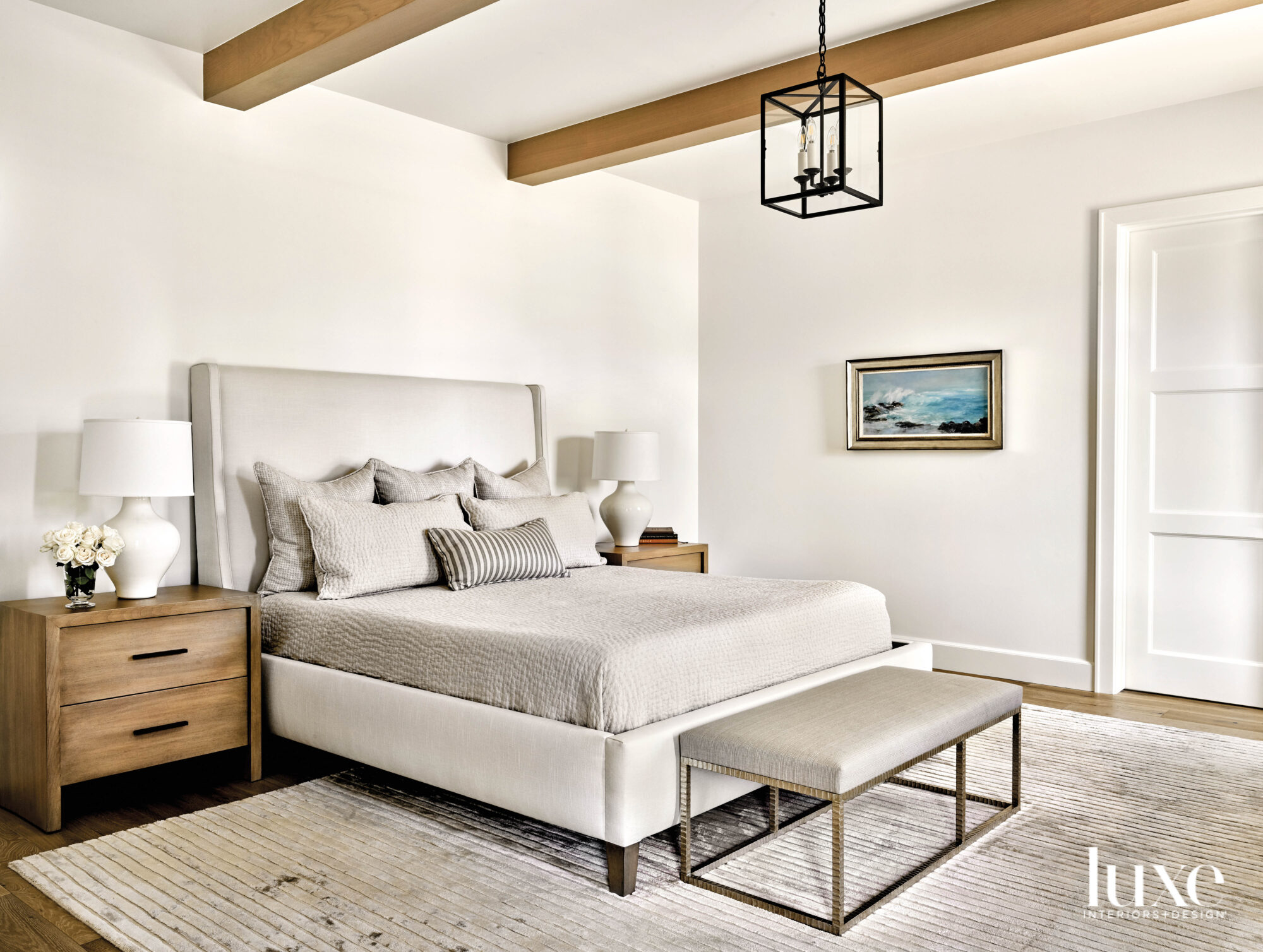 The bed and bed linens are light gray. Light wood ceiling beams match the light wood nightstand.