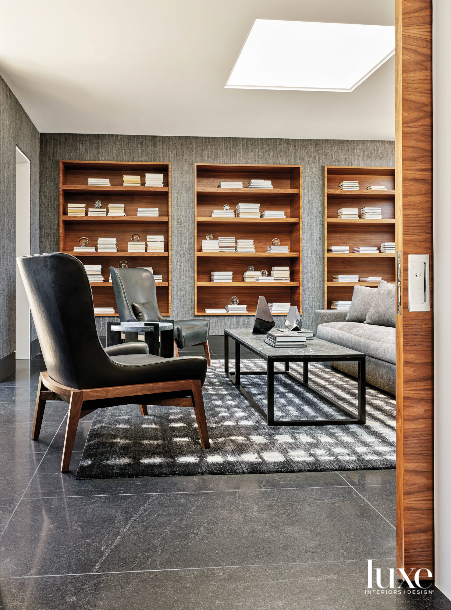 An office with black leather chairs, a gray couch and rows of wood open shelving.