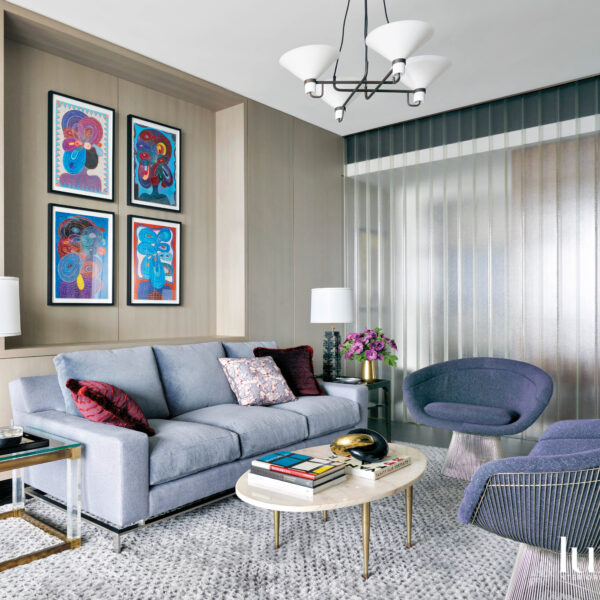A blue sofa and blue midcentury chairs are set off by colorful paintings on the wall above the sofa.