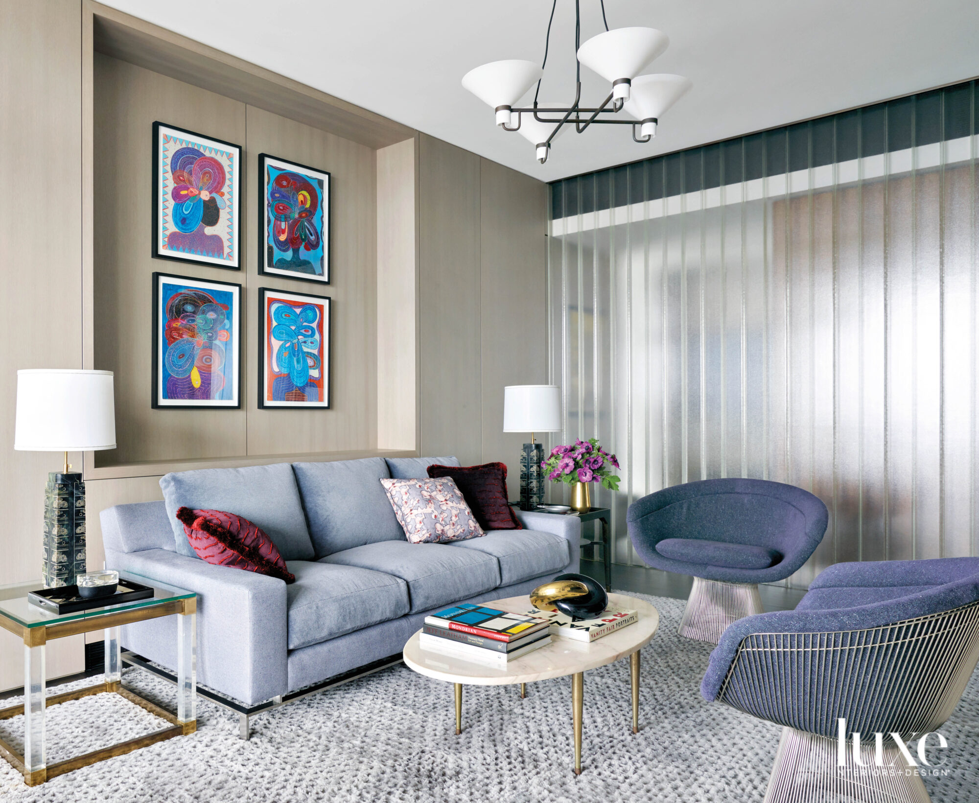 A blue sofa and blue midcentury chairs are set off by colorful paintings on the wall above the sofa.