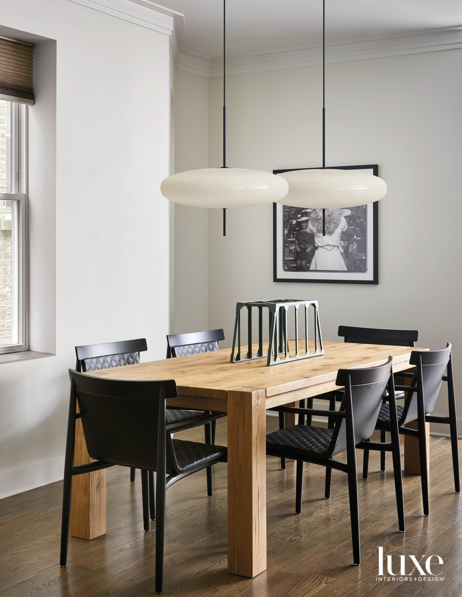 Two pendent lamps hang over a wood dining table surrounded by black chairs.