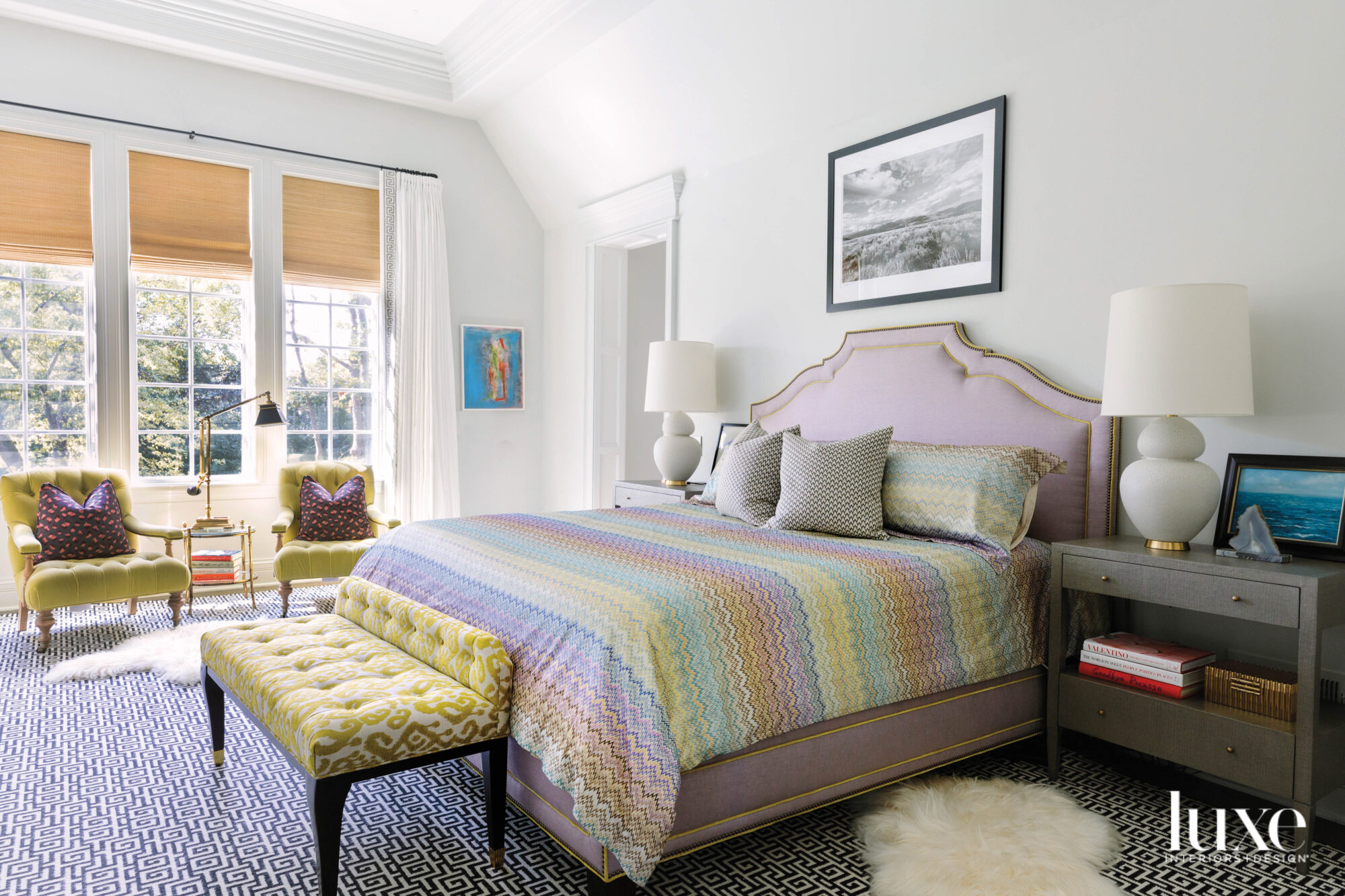 A purple bed has striped purple, yellow and green linens. There are yellow chair in the corner.