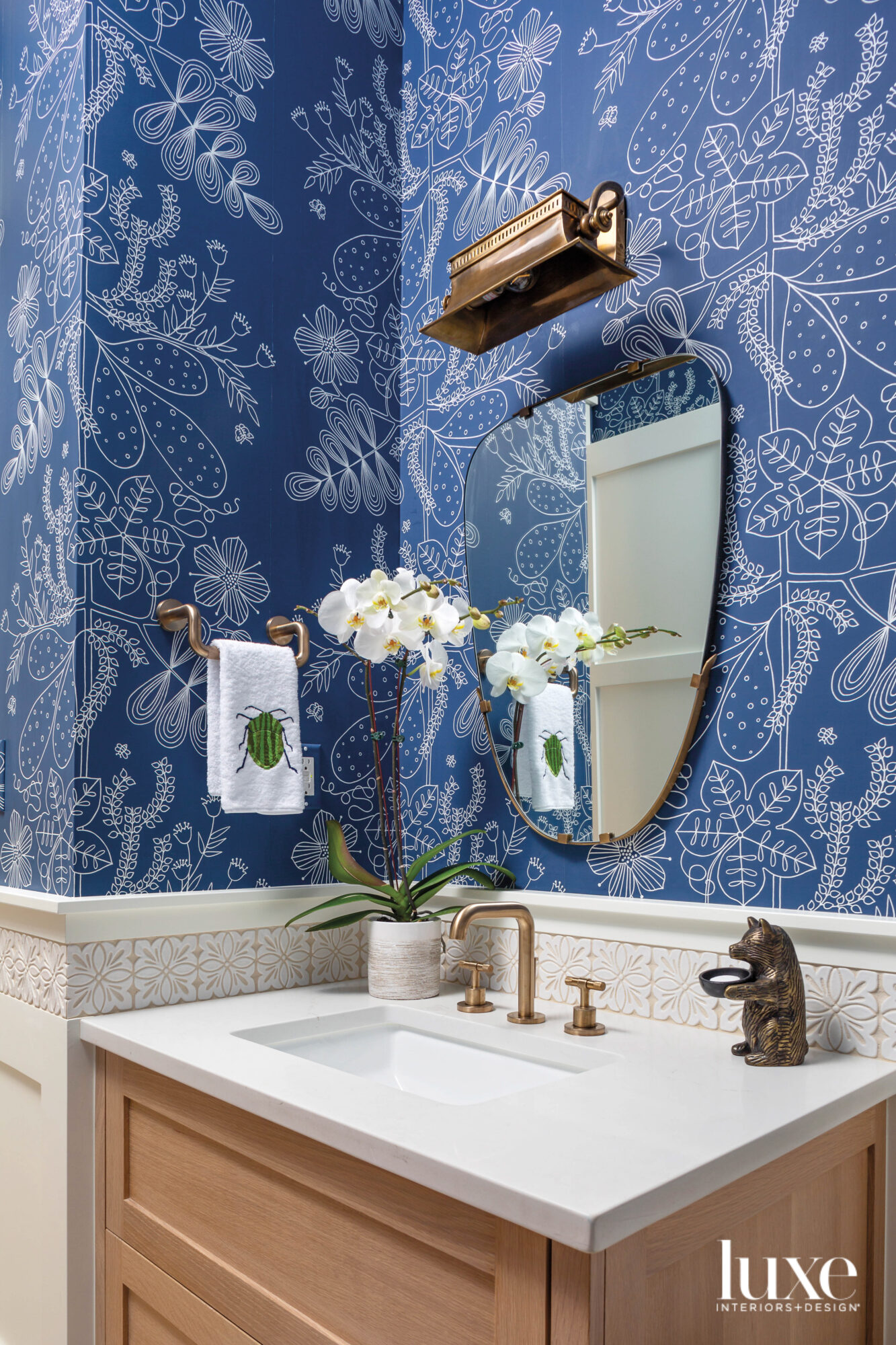 The powder room has a bright blue wallcovering and a brass light fixture.