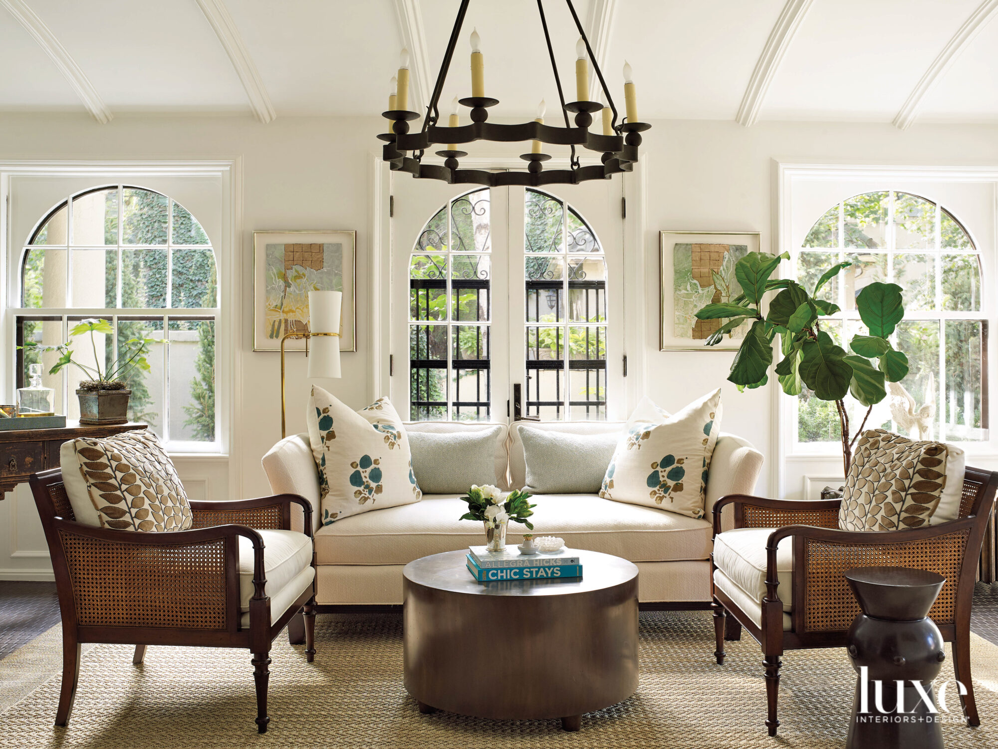 A sunroom has large arched windows and comfortable furniture.