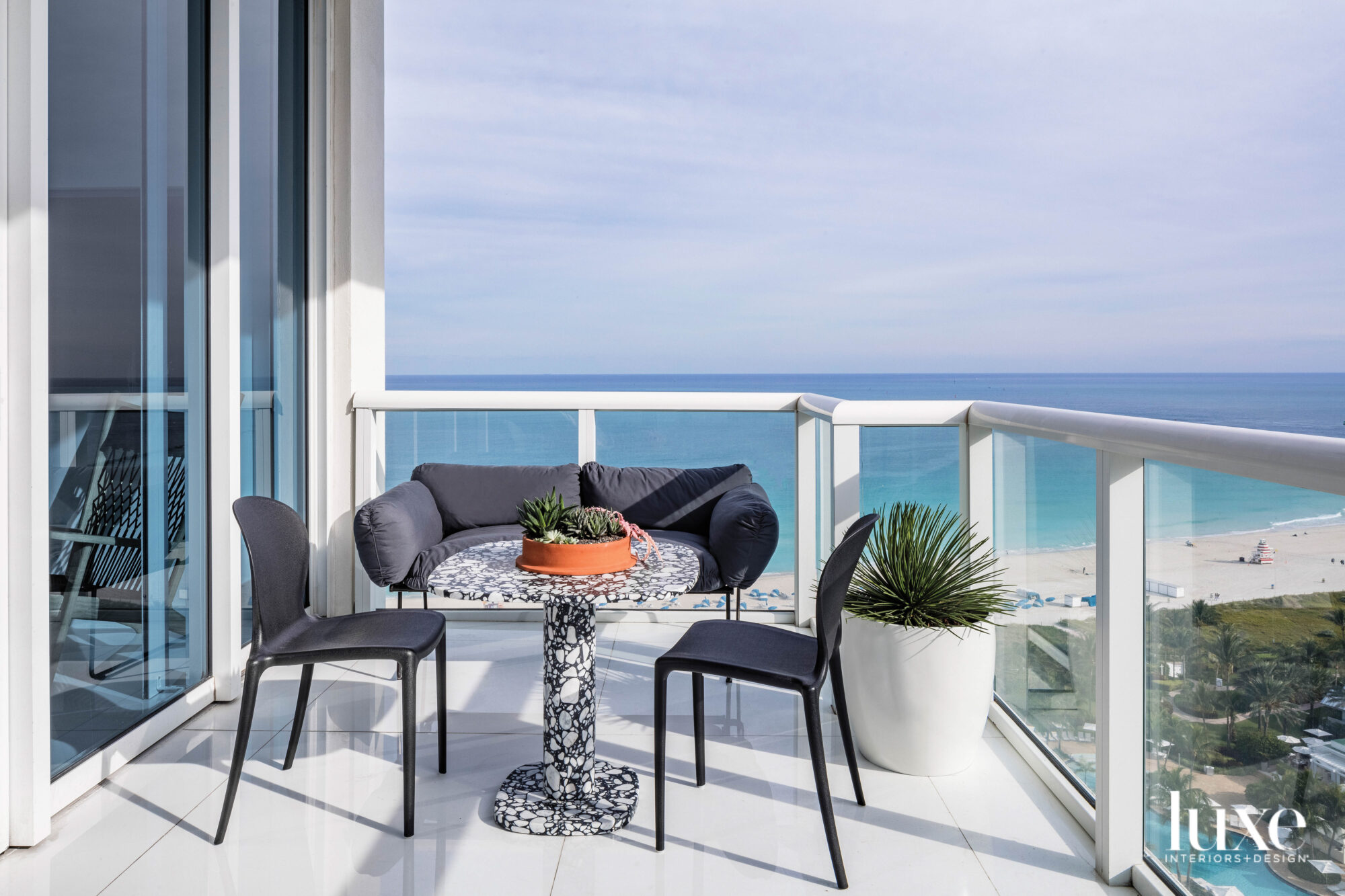 balcony with black loveseat, black chairs and terrazzo table overlooking ocean