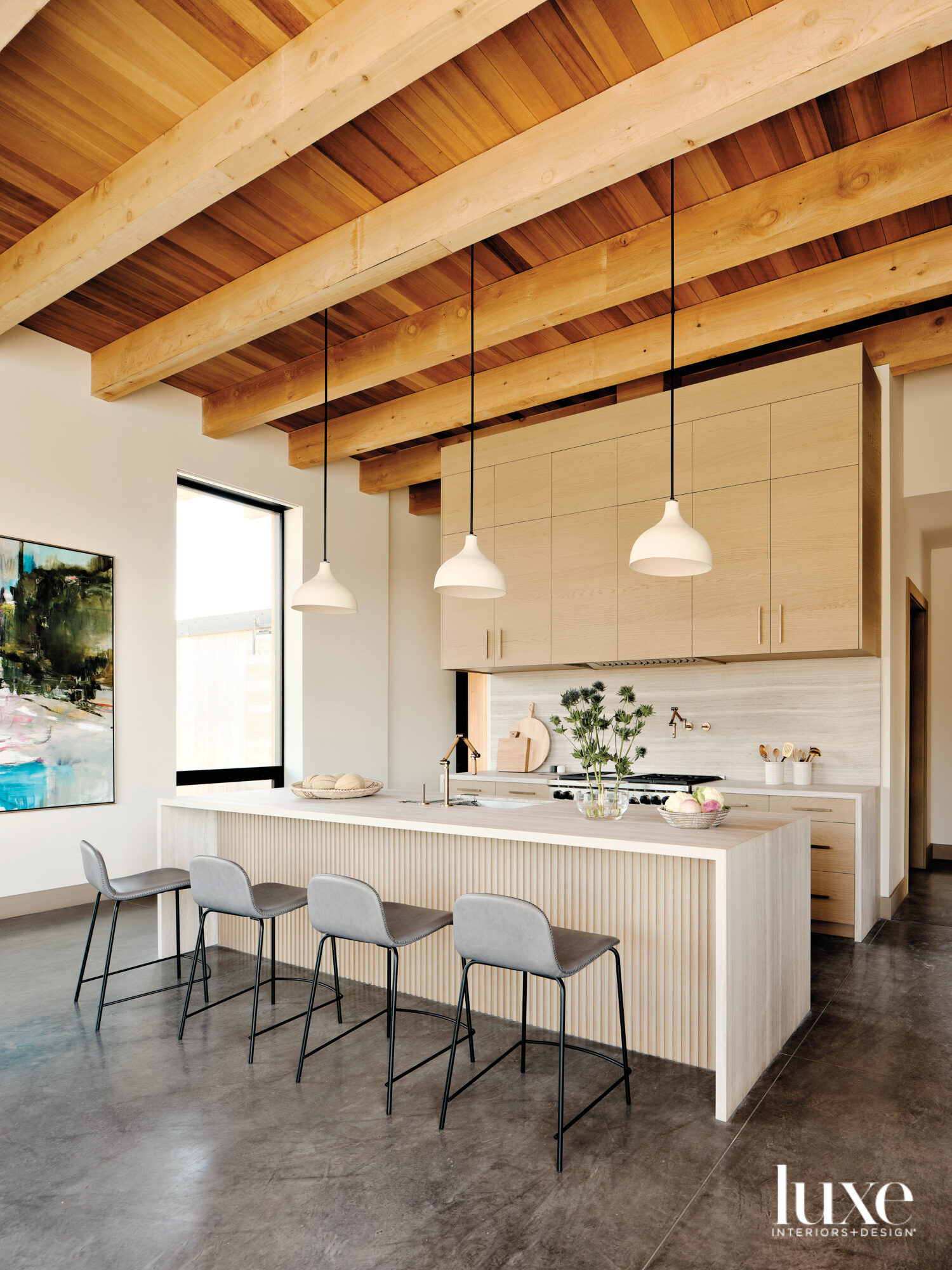 The kitchen has a high, beamed ceiling and light-colored cabinets.