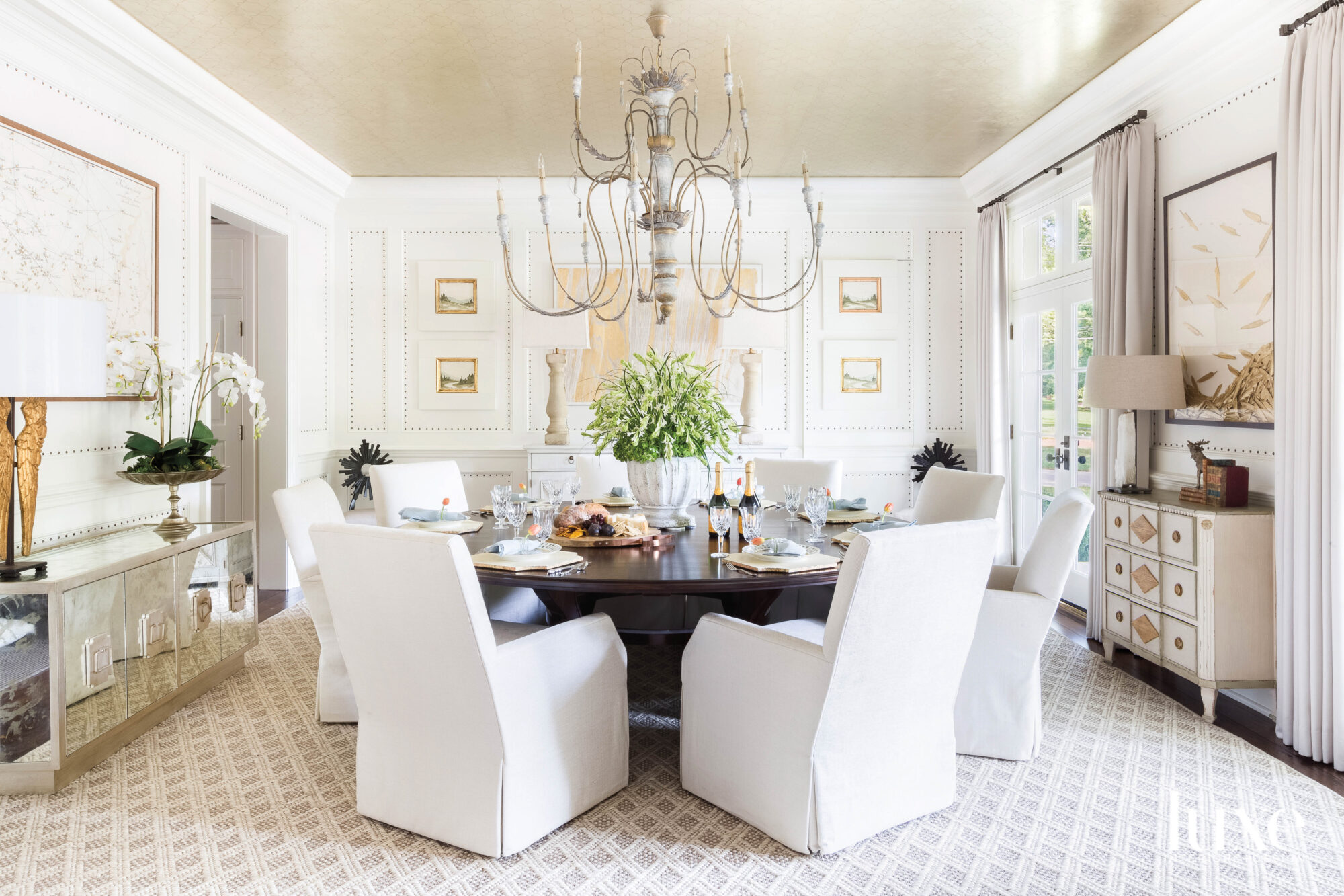 Dining room with metallic ceiling, oversize chandelier and slipcovered dining chairs surrounding a round table
