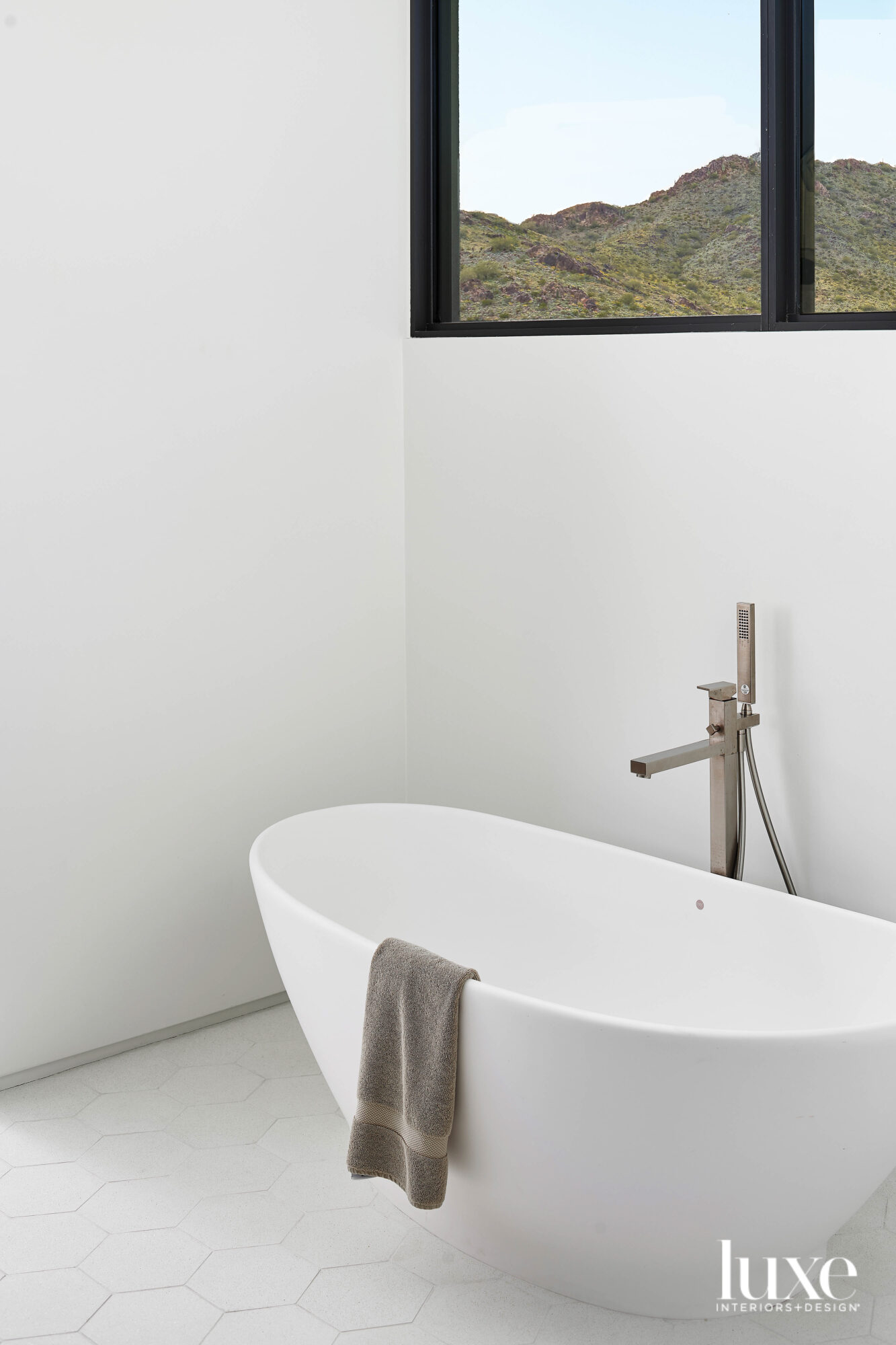 An all-white bathroom with a stand-alone tub and a window looking out at the mountains.