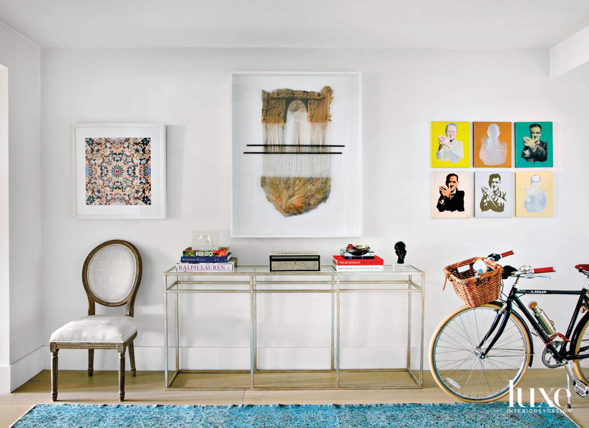 vignette with blue rug, white armchair, glass console, wall artworks and bicycle