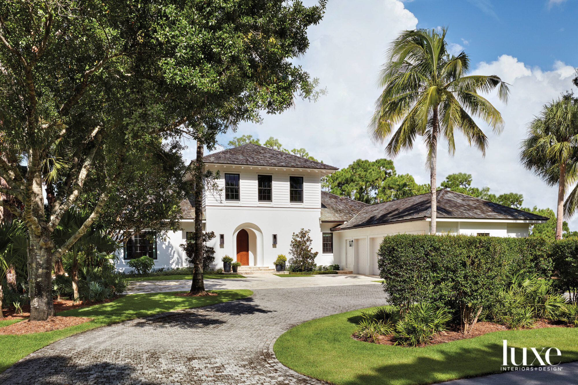 white two-story house with cedar-shingle roof and lush palm tree landscaping