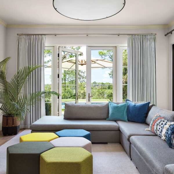 Embrace The Easygoing Elegance Of This New Take On ‘Old Florida’ Style family room with large gray sectional and octagonal ottomans in blue and green