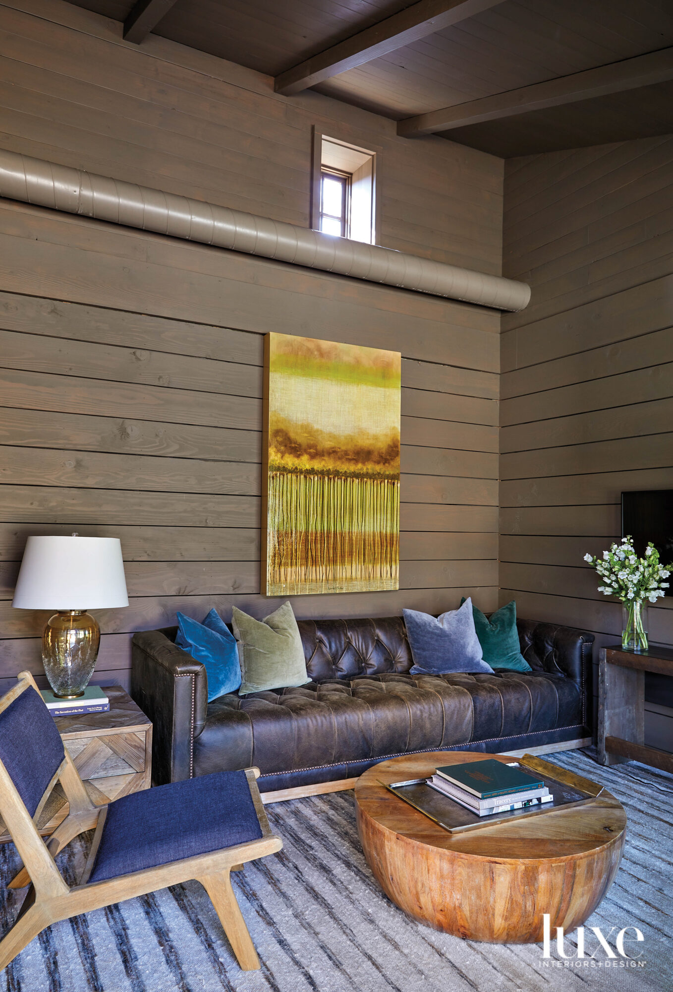 Cozy sitting room with horizontal wood paneling, tufted leather sofa and industrial drum coffee table