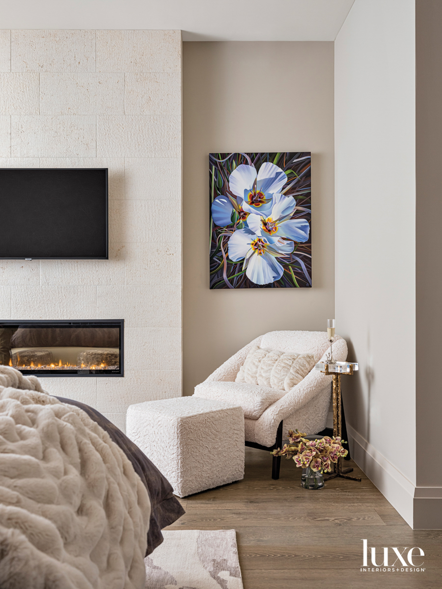 A white chair and ottoman next to a fireplace. Above the chair is a floral painting.