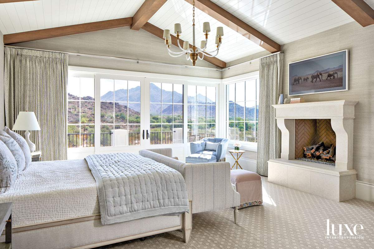 A cream bedroom with a fireplace. The room looks out on the mountains.