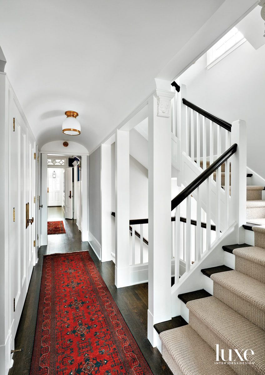 A staircase and a hallway with two red rugs.