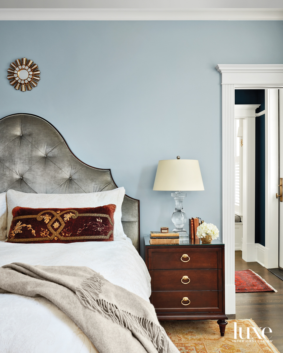 A blue bedroom with a gray velvet bed and gold rug.