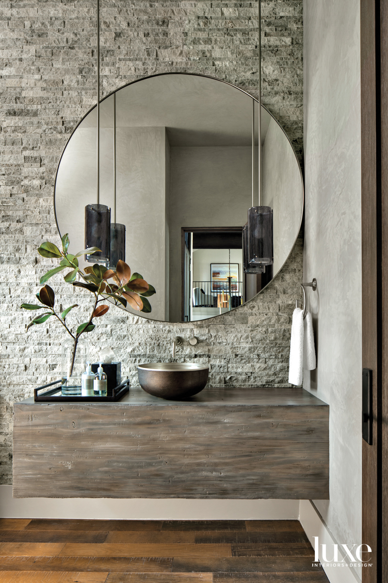 A powder room has a large round mirror over a vanity with a vessel sink.