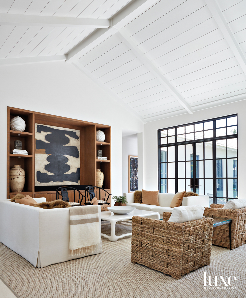 living area with white cathedral ceiling, white and wicker furnishings and wood console with black and white artwork