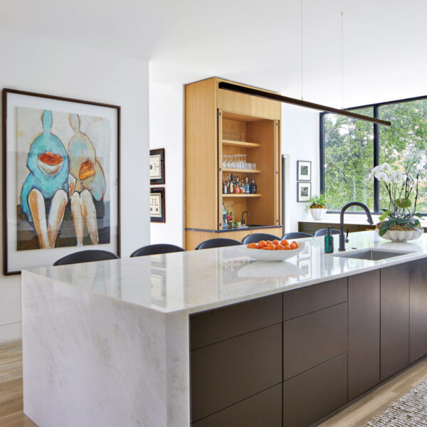 A Lush Tree Canopy Inspires A Timber Merchant’s Own Mod Home Modern kitchen with waterfall marble countertops, built-in bar and abstract figurative artwork on wall