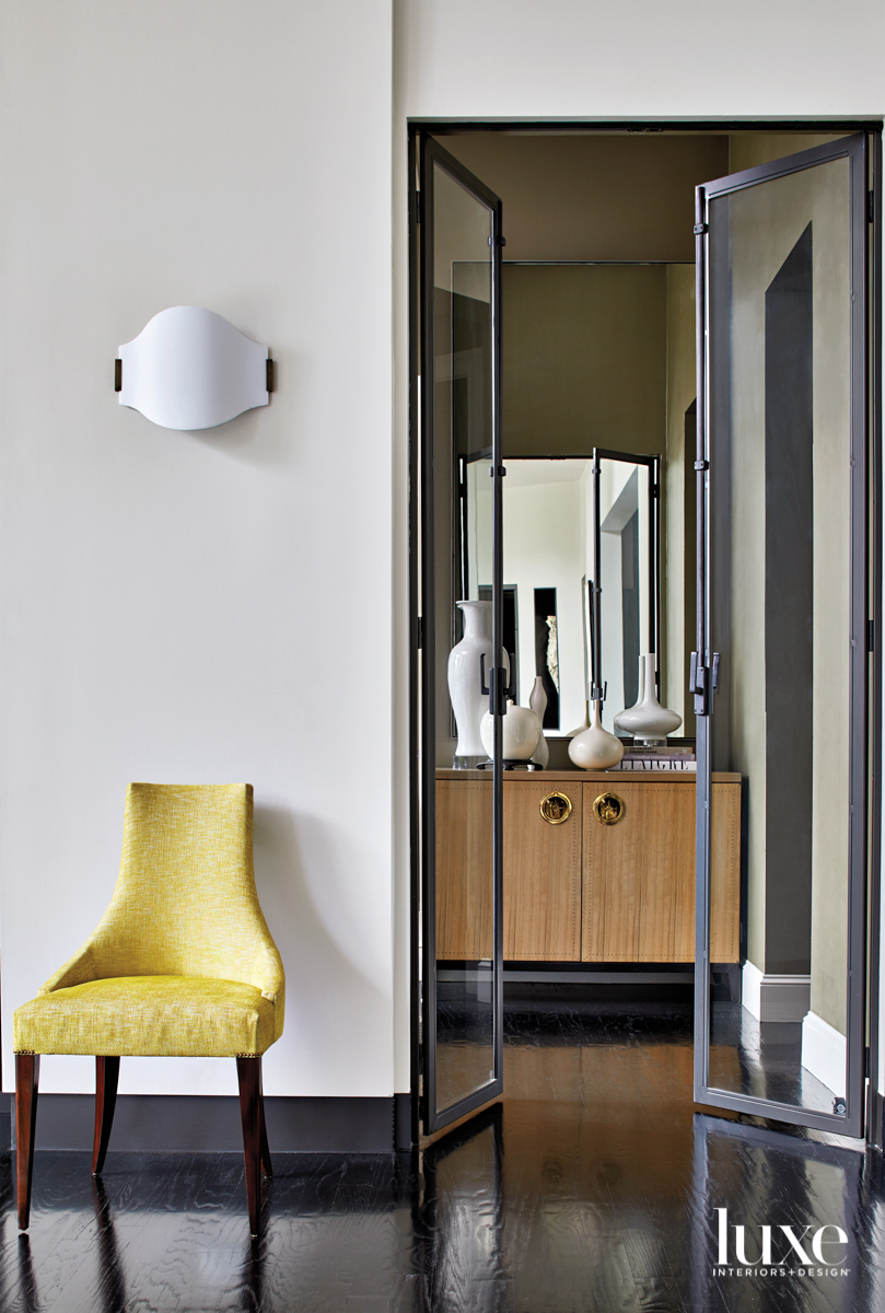 Graphic vignette with sculptural citron side chair, simple sconce, and a cabinet topped with white vessels