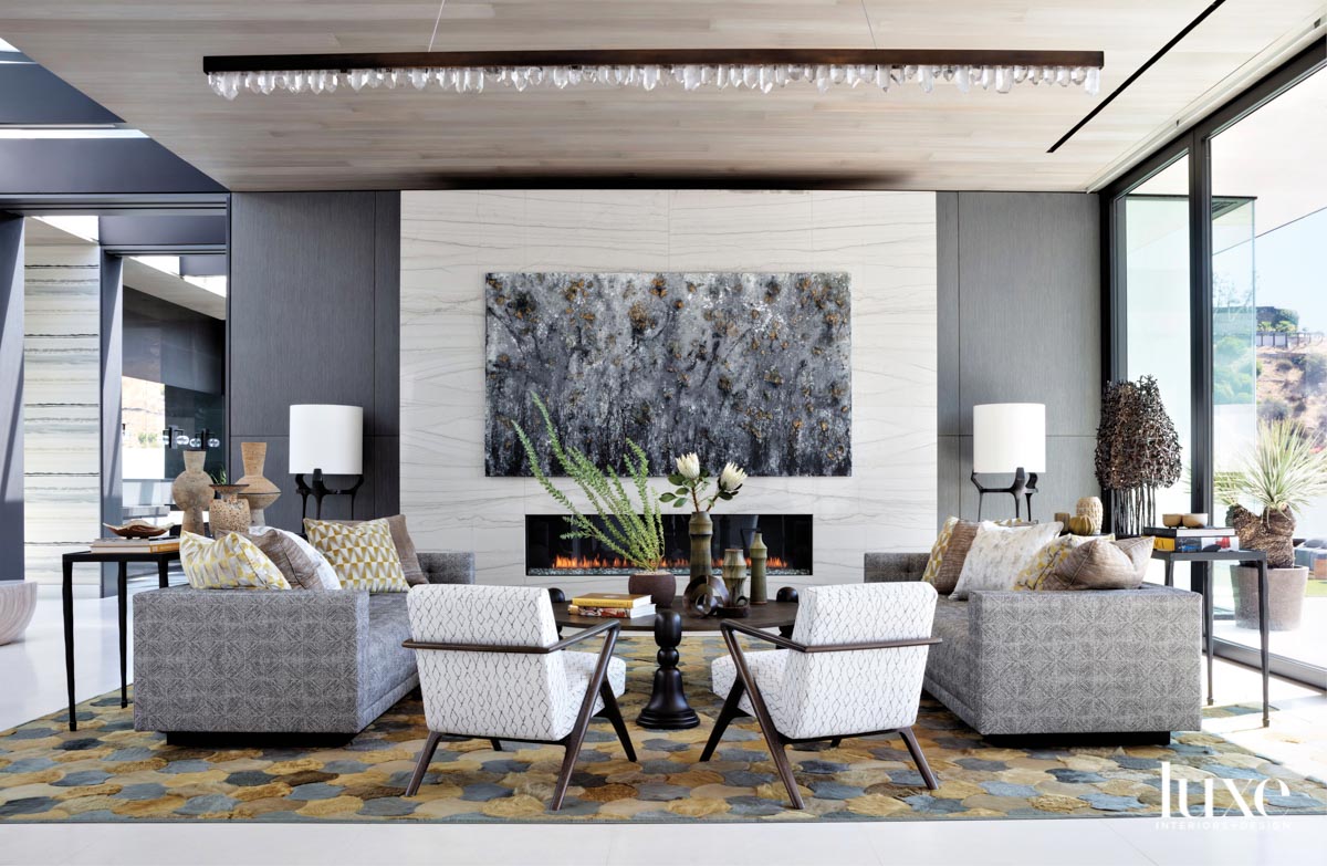 View of living room facing a fireplace with a large artwork hanging above, pair of sofas and two lounge chairs