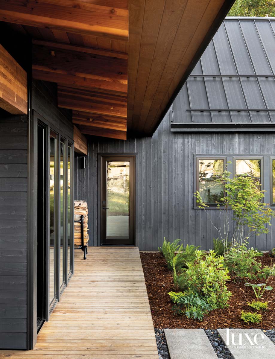 Wood walkway leading to front door of house with black siding and roof