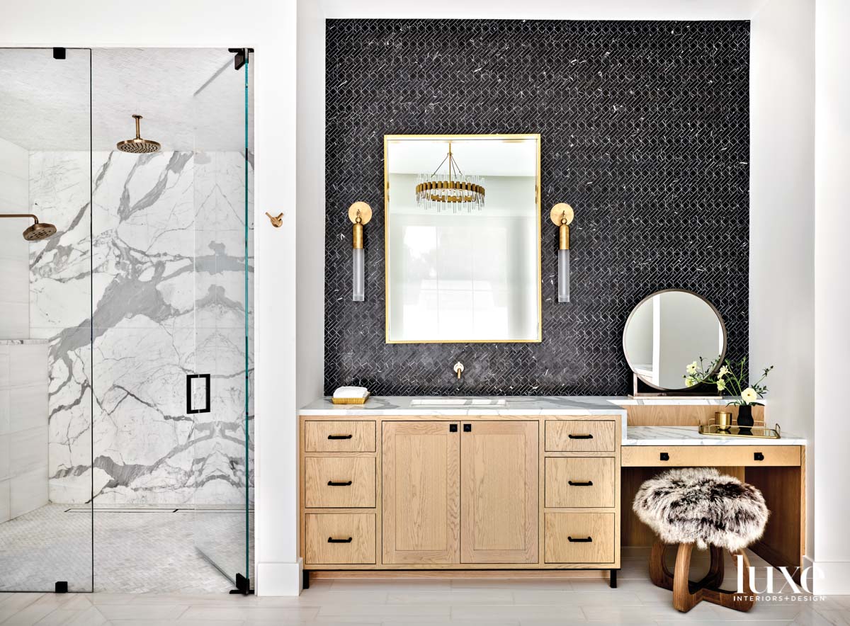 A bathroom with a light oak vanity and black tile on the wall.