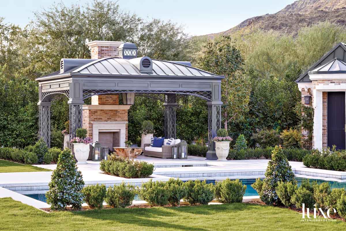 A fireplace pavilion with seating that sits next to the pool. You see mountains in the background.