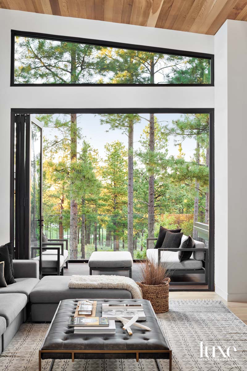 A seating area that opens to a patio overlooking trees. The seating in both spaces is black and gray.