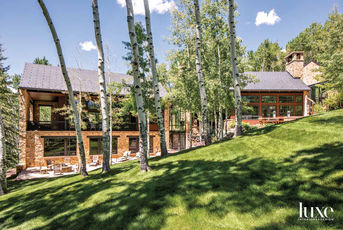 The home is surrounded by grass and aspen trees.