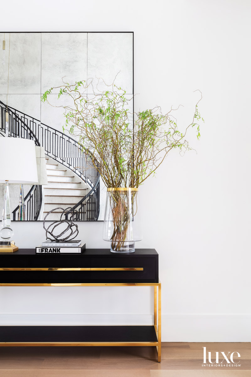 Vignette with sleek black console, glass lamp and large mirror reflecting the staircase