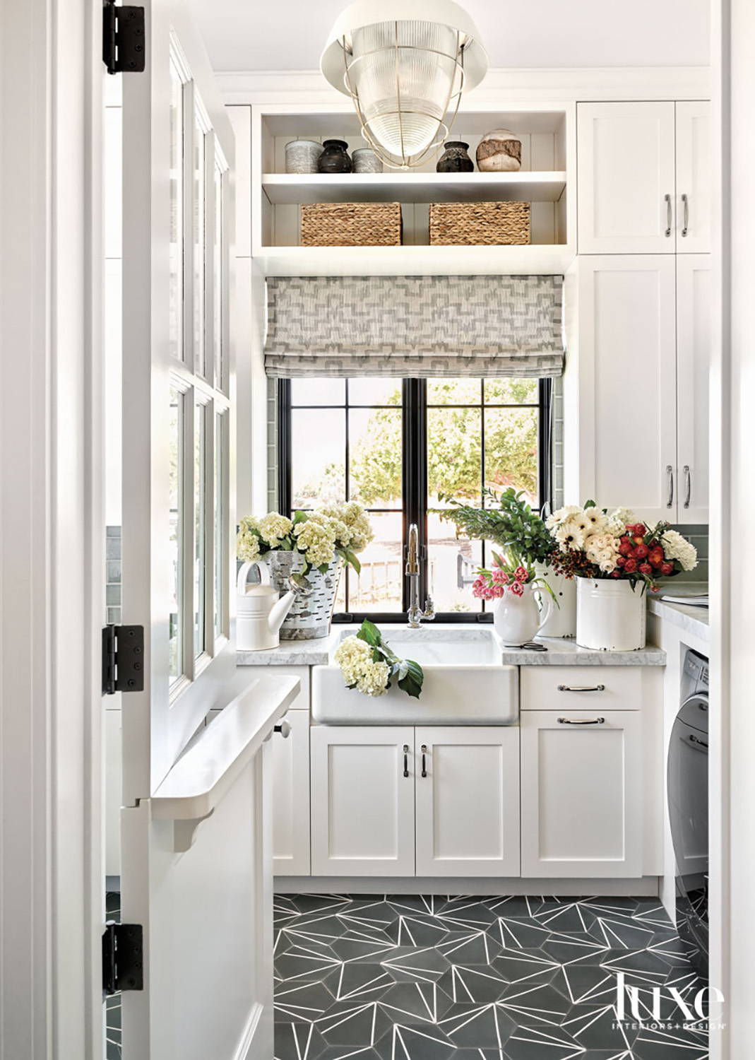 A laundry with gray-tile geometric floor, white cabinetry and a farmhouse sink.
