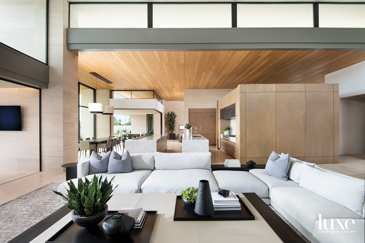 sectional sits around leather coffee table in a modern organic living room that opens to a kitchen