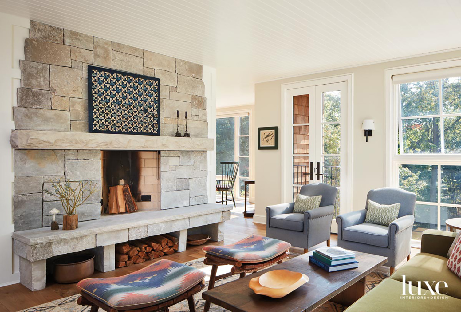A living room with a large stone fireplace, two blue armchairs, a green sofa and two stools