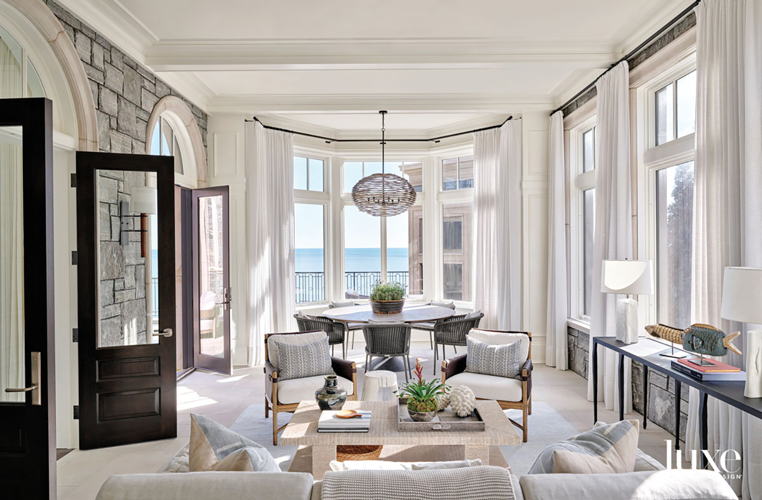 A round table on one side of a sun room that looks out on the lake. A round chandelier hangs above.