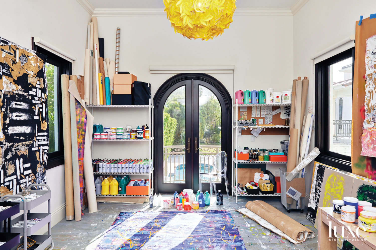 aidan marak's artist studio, with a work on the floor, arched doorway and yellow chandelier above