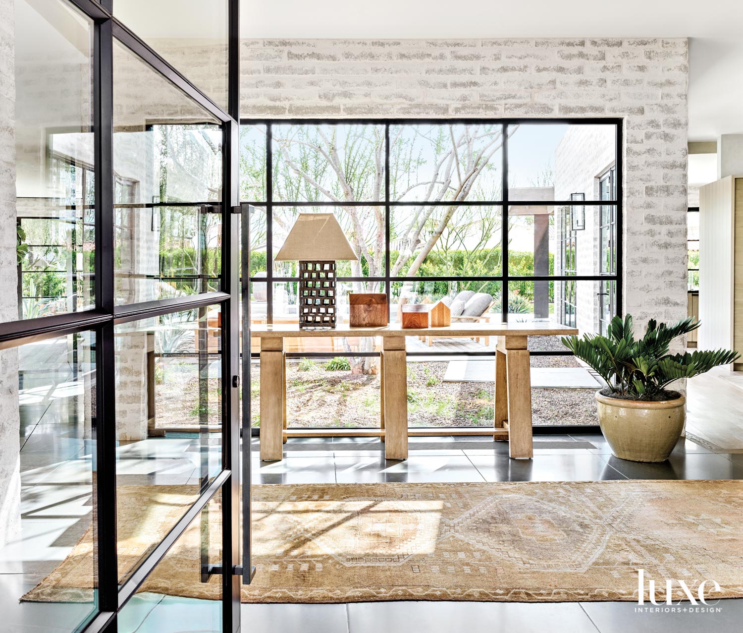 An entry-way with steel-and-glass windows, a light wood console and an antique rug.