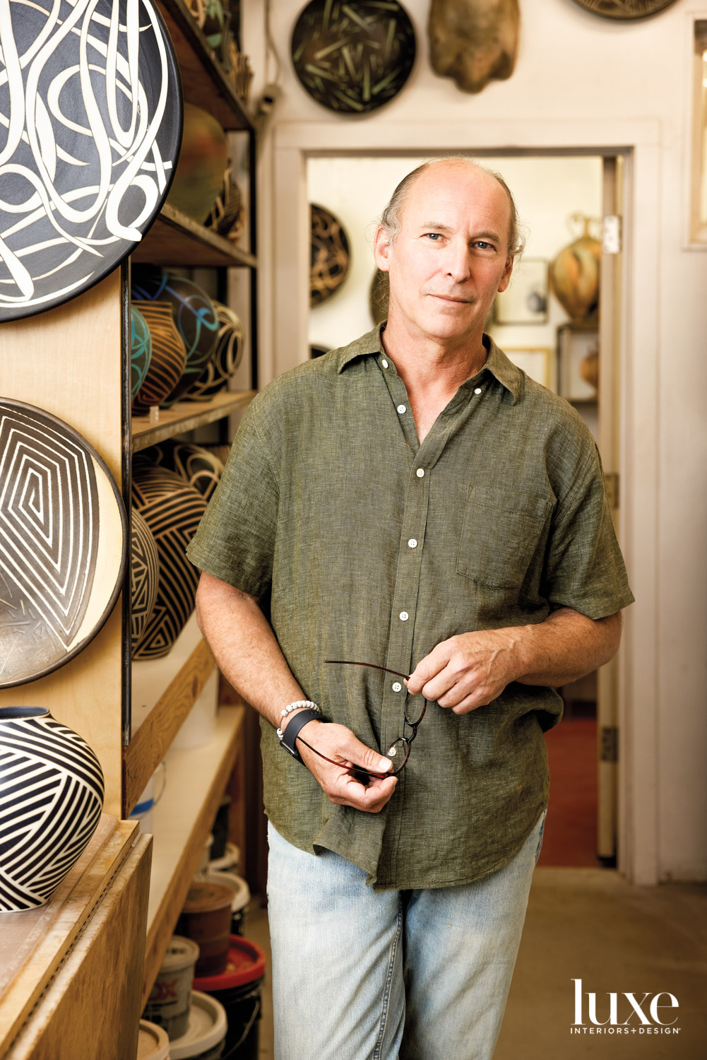 A man standing in a studio surrounded by ceramics.