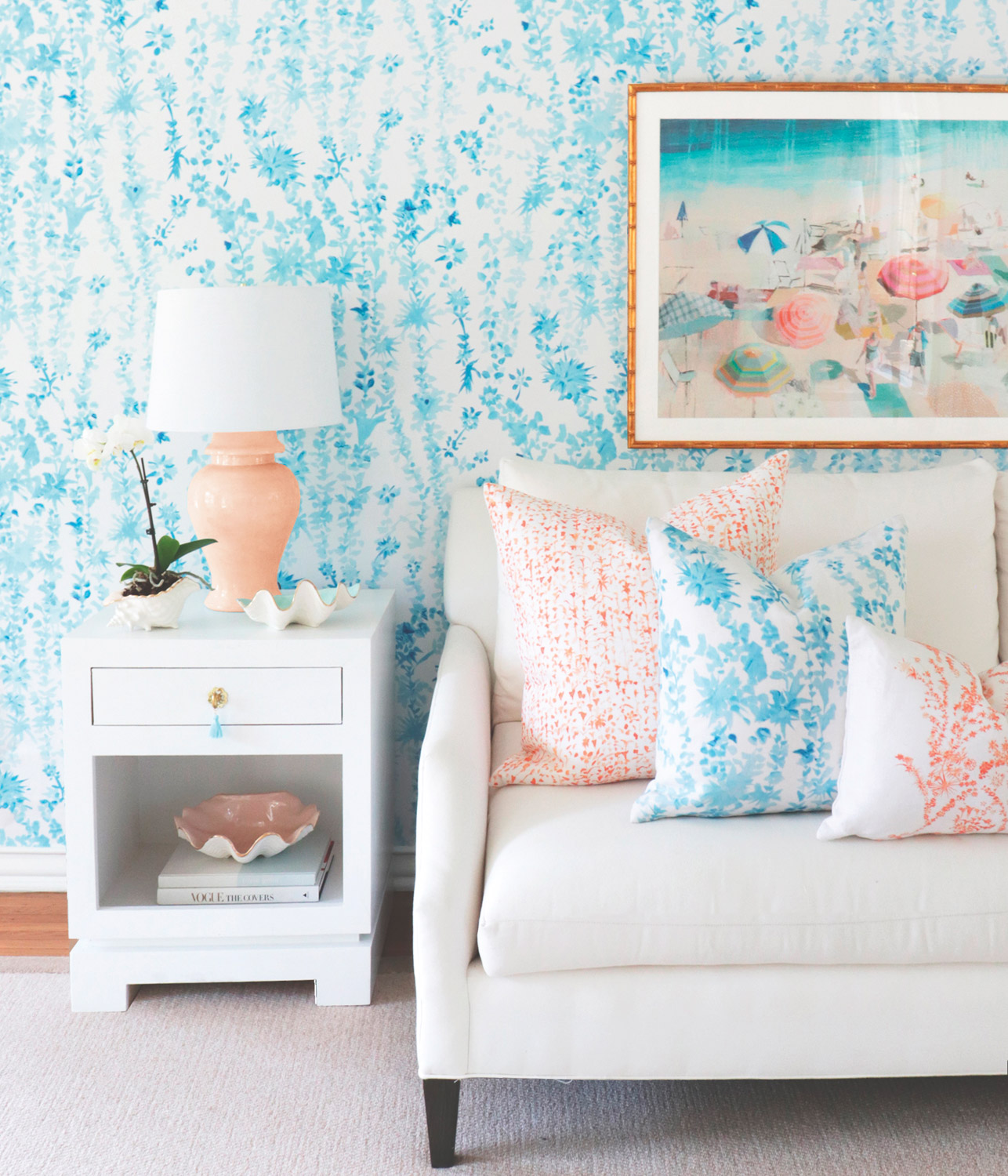 A living room setting with blue and coral patterned pillows, blue wallpaper and coral lamp 