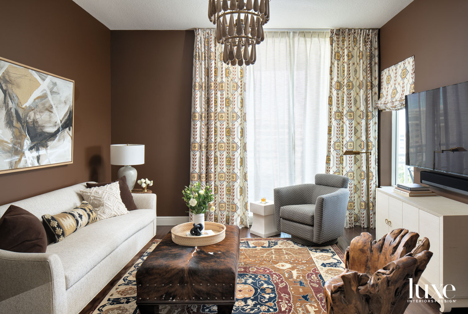 den with chocolate brown walls, white sofa, gray armchair Persian rug and patterned draperies