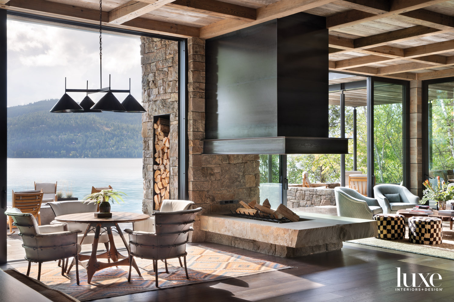 Living area featuring a central open fireplace with a games table and chairs on one side and lounge chairs on the other with views facing the lake