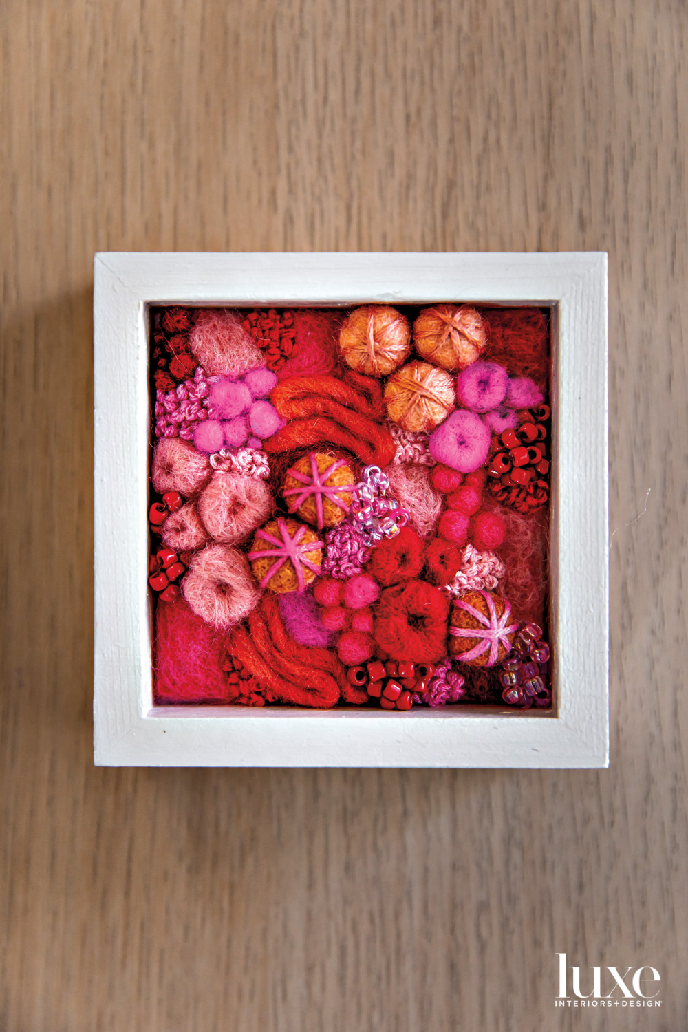 Small framed artwork composed of felted forms in reds, oranges and pinks
