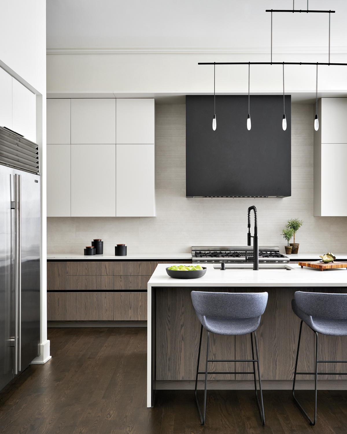 Sleek white kitchen with a black hood over the range, and gray stools by the island