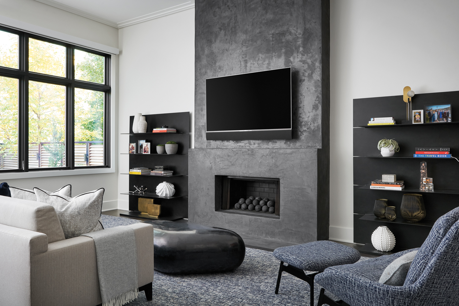 A muted living room in gray and black tones including a concrete fireplace, a black stone coffee table and steel bookcases.
